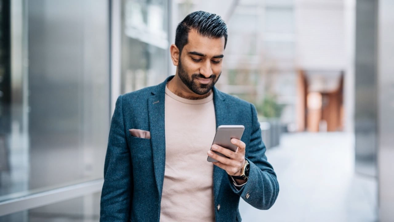 Smartly dressed Asian man smiling down at phone