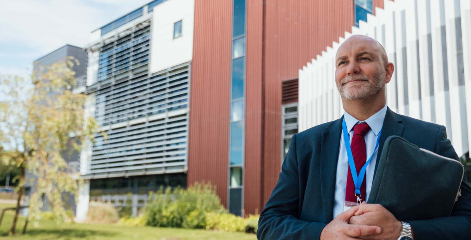 Male teacher standing outside school building holding clipboard