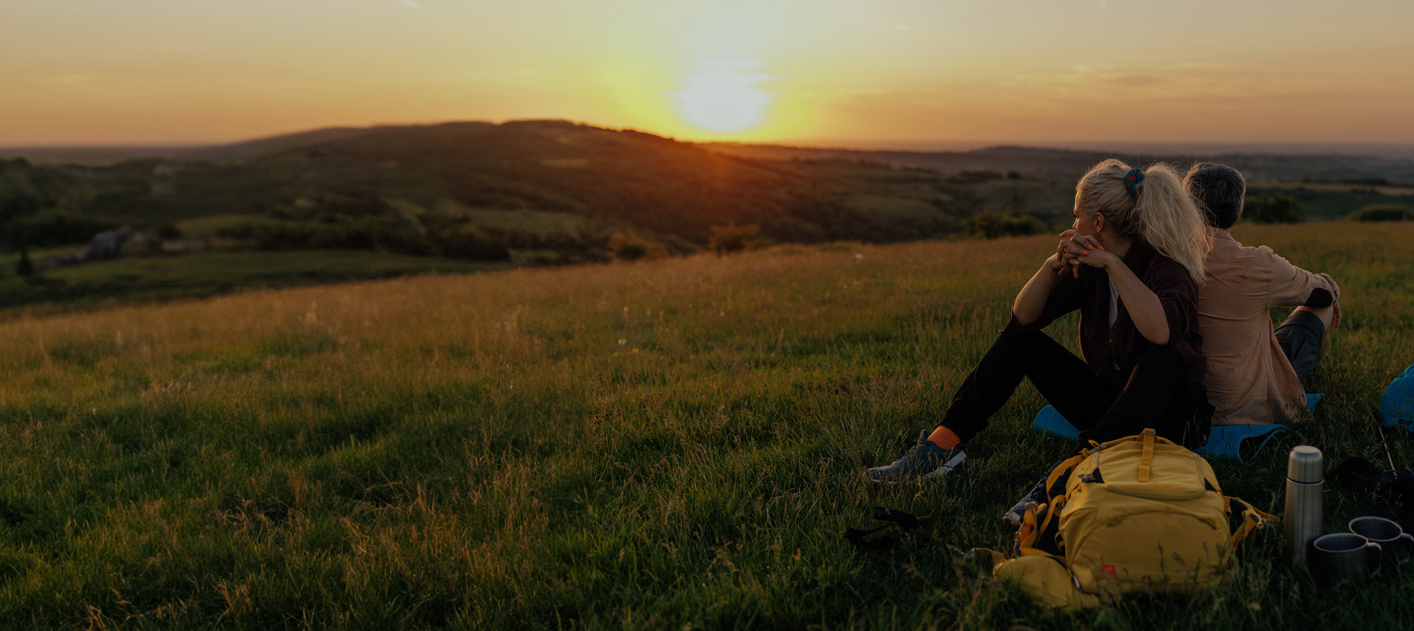 Couple sitting back to back on field watching sunset