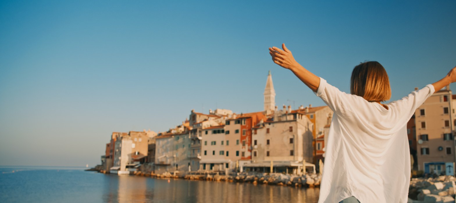 Woman standing on beach front with open arms looking out at sea