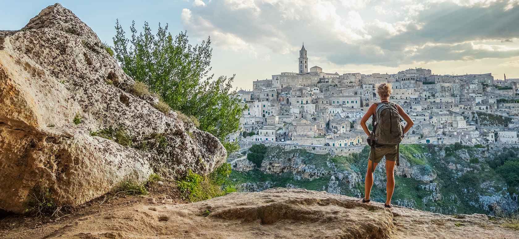 Woman standing on hill with backpack looking at scenic city views