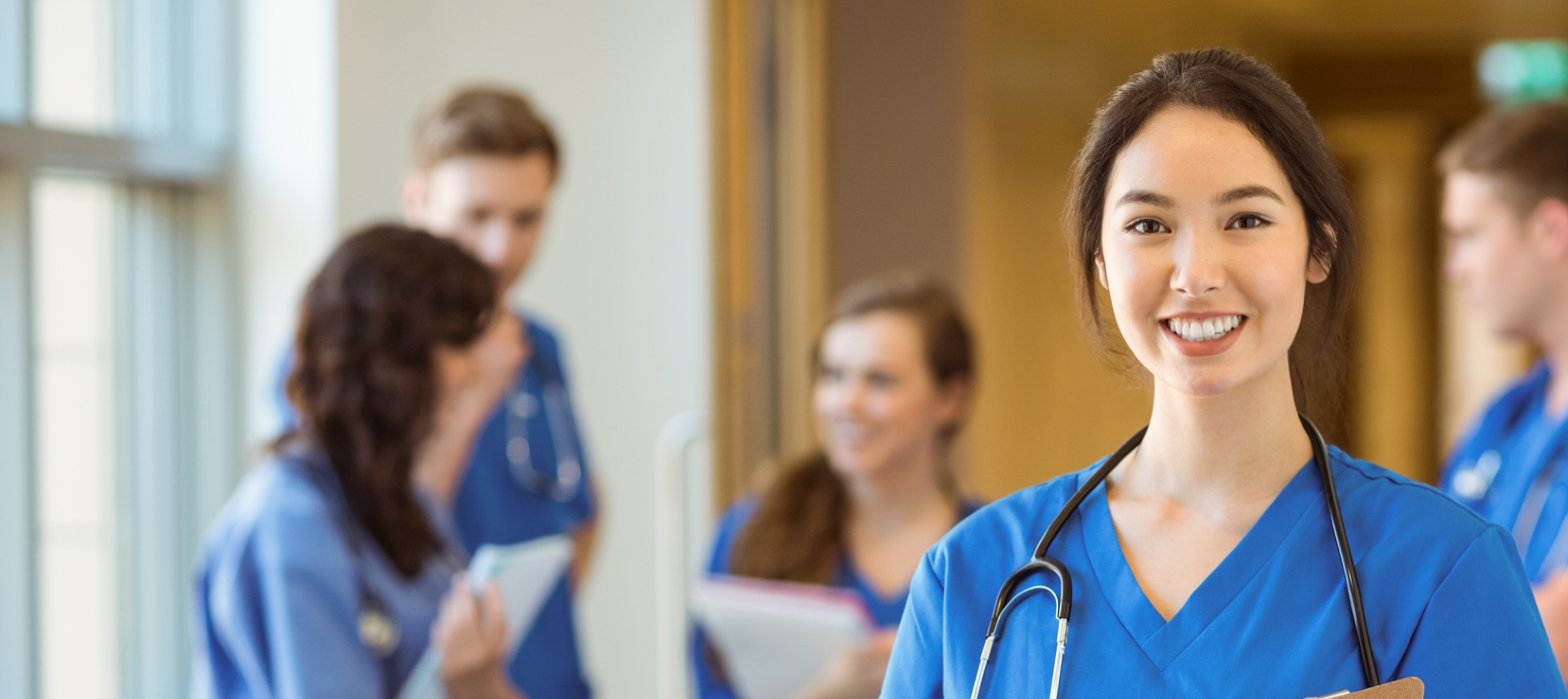 Young female medic standing in corridor smiling wearing blue scrubs