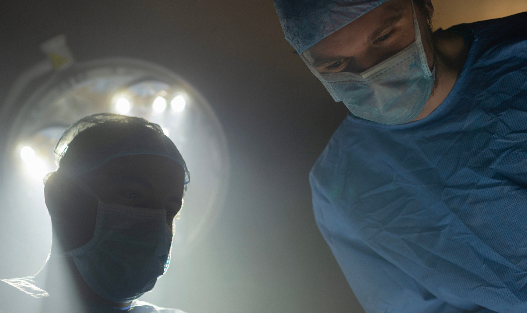 Two surgeons leaning over a patient