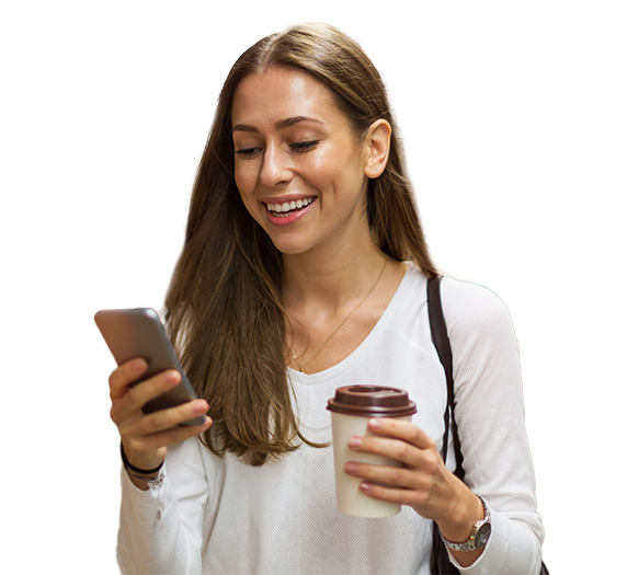 Woman holding a coffee cup on one hand and phone in another, looking down at the phone smiling